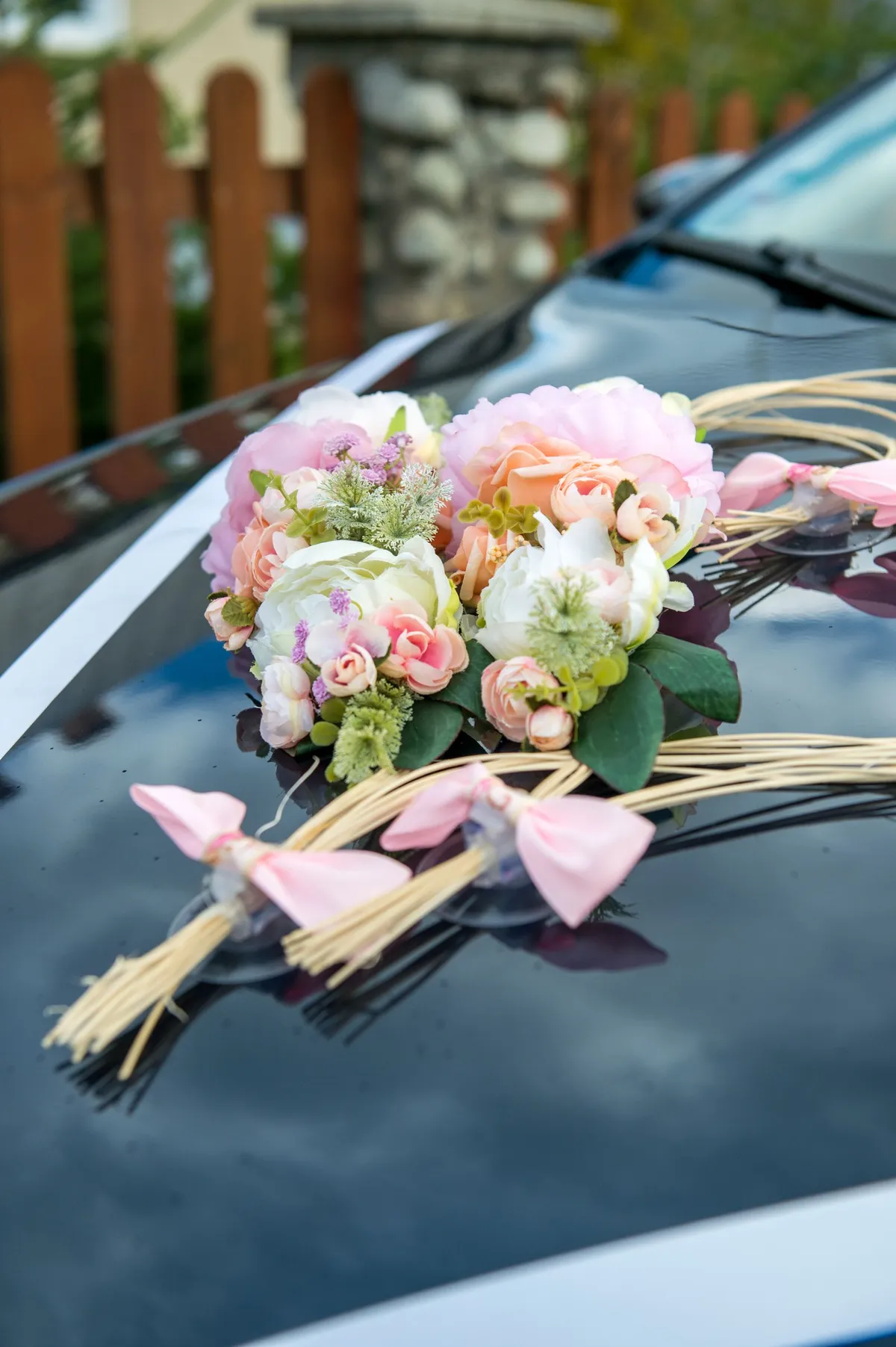 Arranjo de flores claras e laços cor-de-rosa sobre o capô de um carro de casamento