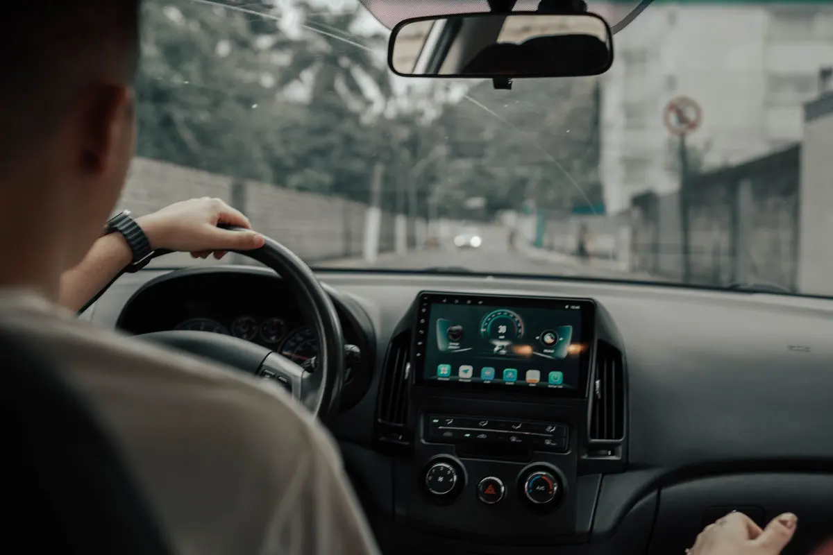 Driver with hands on the steering wheel, driving a car along a tree-lined street