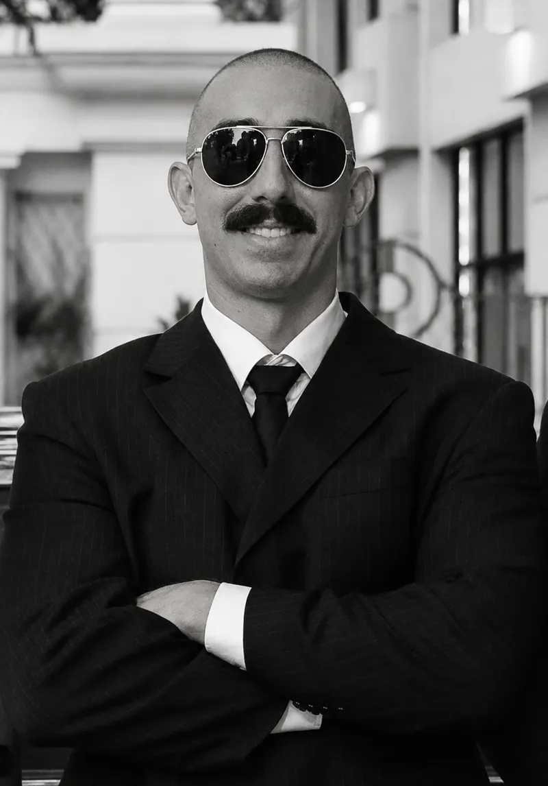 Executive driver in a pinstripe suit, tie and sunglasses, arms crossed, in a black-and-white portrait